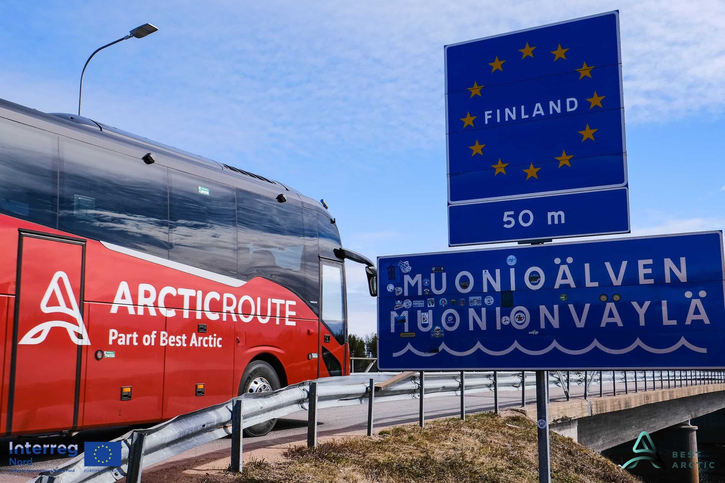 Autocar Arctic Route passant le panneau frontalier finlandais au bord de la rivière Muonio