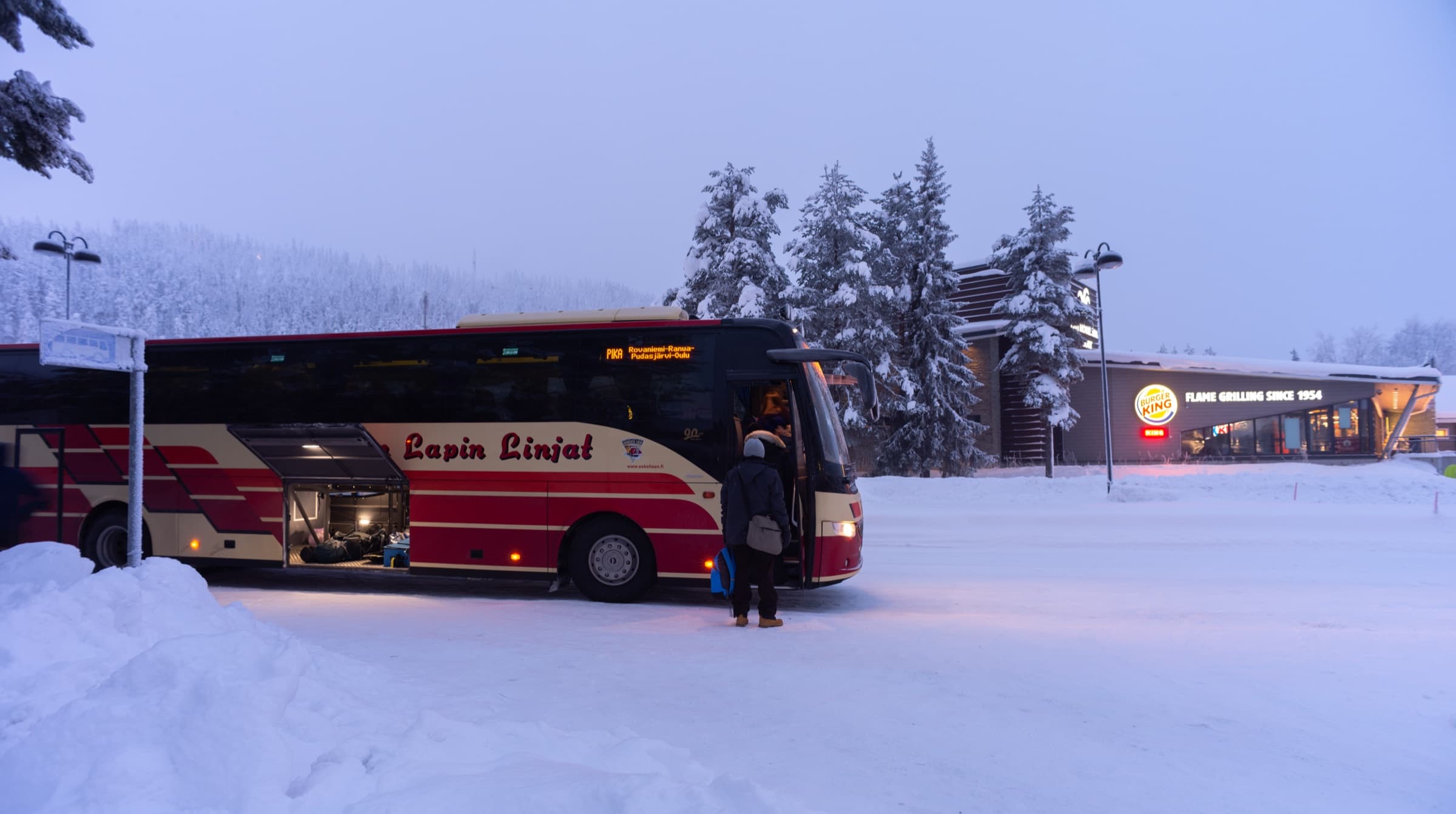 Passager montant dans le bus à un arrêt enneigé au bord de la route à Levi au crépuscule
