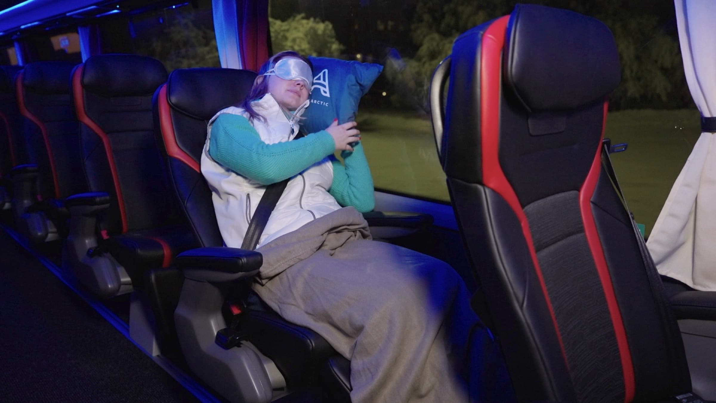 Passagère endormie sous une couverture dans un siège inclinable de l'Aurora Express, masque sur les yeux