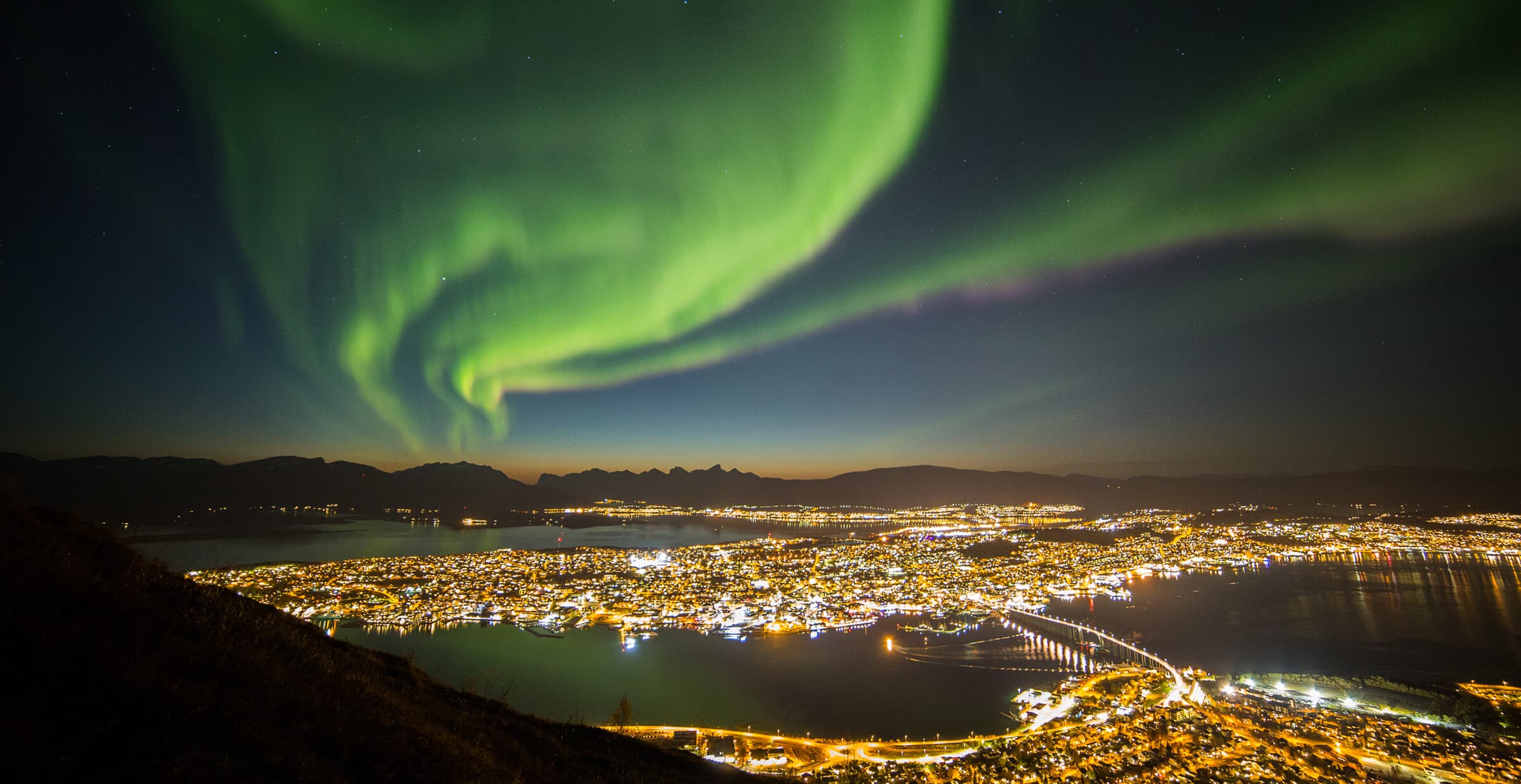 Nordlichter über den Lichtern von Tromsø und den umliegenden Fjorden
